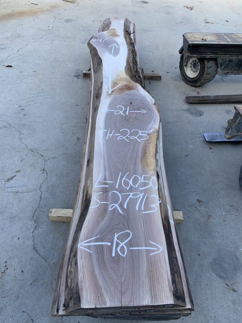 A raw wooden log slab with markings laid on a concrete floor.