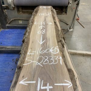A large wooden slab marked with dimensions and weight in a workshop.